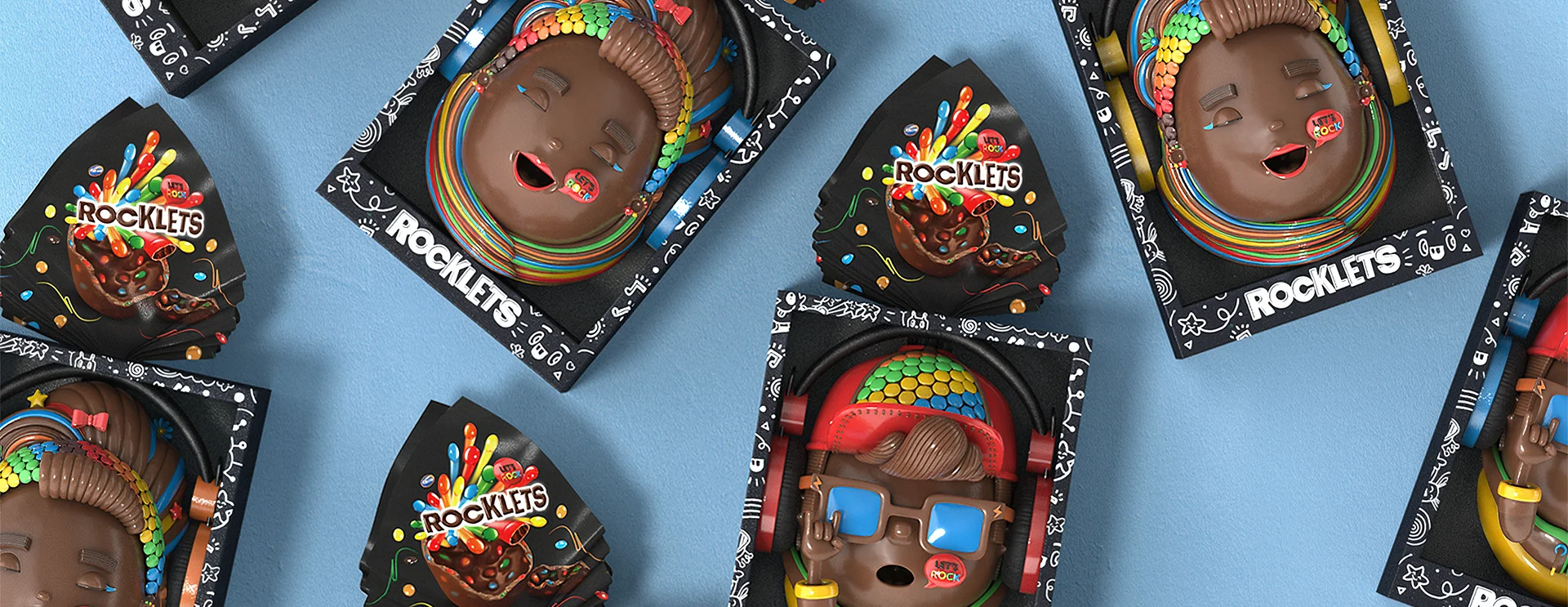 Rocklets_Still01 Rocklets Easter egg packaging featuring colorful chocolate characters with candy accessories, arranged on a blue background.