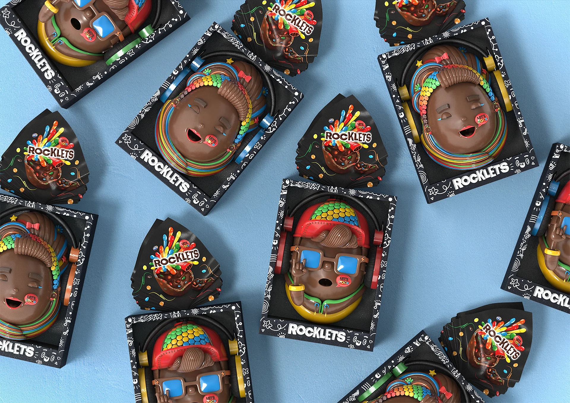 Rocklets_Still010 Overhead arrangement of Rocklets Easter egg packages featuring two chocolate character designs on a light blue background.